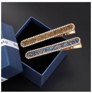 Detail of luxury rhinestone hair clips in gold and blue tones with gift box packaging