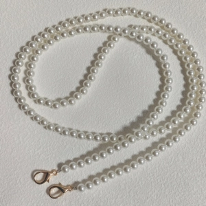 Close-up of elegant pearl chain with gold lobster clasps on a textured beige background
