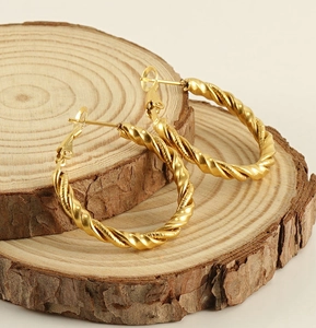 Detail of gold spiral twisted hoop earrings placed on a natural wooden display