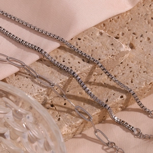 Detailed close-up of stainless steel box chain and paperclip chain on a neutral stone base