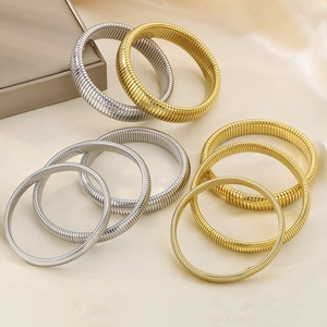 Detailed view of layered gold and silver ribbed spring bangles on champagne silk fabric