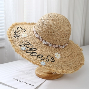 Detail of hand-woven raffia sun hat with 'Sun please' embroidery and floral lace trim
