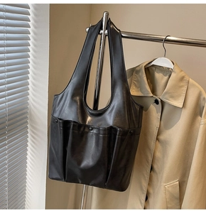 Detail of a large black PU leather tote bag with exterior pocket hanging on a metal hanger