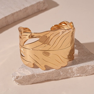 Détail du bracelet manchette feuille dorée avec textures nervurées sur fond de pierre