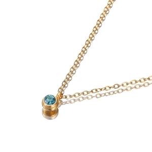 Polished gold necklace with round blue zircon pendant on white reflective surface