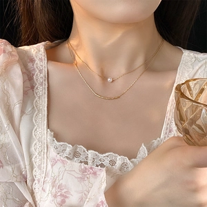 Close-up of model wearing a double-layered gold necklace with a white baroque pearl pendant