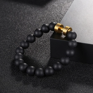 Détail du bracelet en perles noires mates avec un pendentif haltère doré sur l'emballage