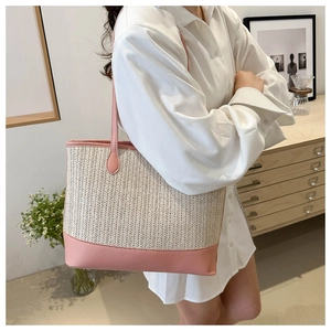 Chic beige woven tote bag with pink leather trim worn by a model in a minimalist room