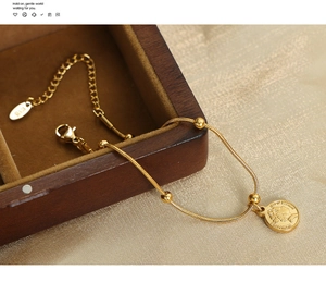 Detail of 18K gold-plated snake chain bracelet with queen coin pendant and bead charms