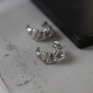 Macro view of silver C-shape earrings with irregular molten lava texture and wrinkles