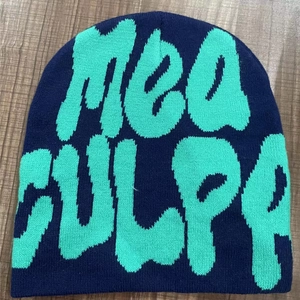 Navy blue knitted beanie with Mea Culpa embroidery in light blue on wooden background