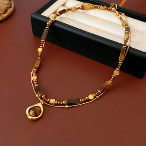 Dettaglio collana dorata a due strati con perline e ciondolo in pietra occhio di tigre