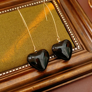 Macro shot of vintage black heart pendants with gold hooks on a rustic wood frame