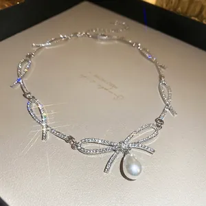 Sparkling diamond bow necklace featuring a white teardrop pearl pendant in silver finish