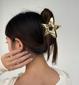 Detail of a large gold star-shaped metal hair claw clip with a hammered texture finish