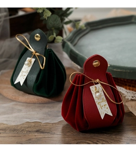 Close-up of velvet and leather gift bags with gold cords and pearl charms on wood