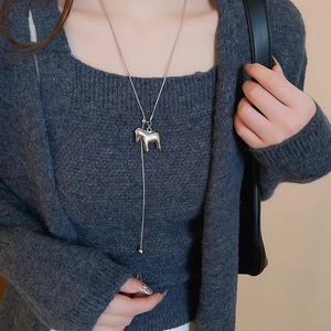 Close-up of a silver horse pendant on a sleek chain over a dark grey sweater texture