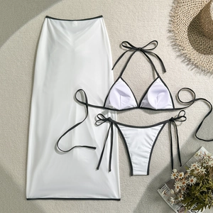 Three-piece bikini set with contrast black trim and matching sheer beach skirt on a rug