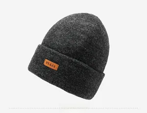 Detailed close-up of dark grey knitted winter beanie featuring an orange leather logo patch