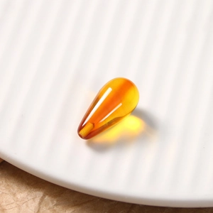Macro shot of a vintage amber teardrop resin bead on a white ceramic plate texture