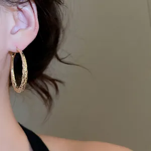 Elegant gold twisted hoop earrings with textured finish worn by a model on casual occasion