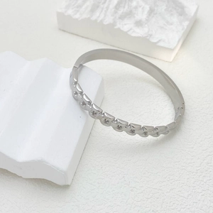 Detail eines silbernen Titanstahl-Armbands mit geometrischem Schuppenmuster auf Stein