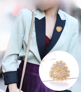Detailed close-up of Baroque gold heart brooch with crystals on green blazer