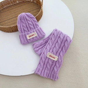 Detail der lila Strickmütze und Schal für Kinder mit Buchstaben-Patch für den Winter