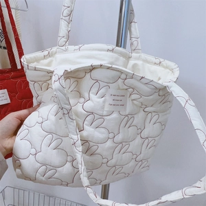 Close-up of white quilted tote bag featuring red rabbit embroidery and French fabric label