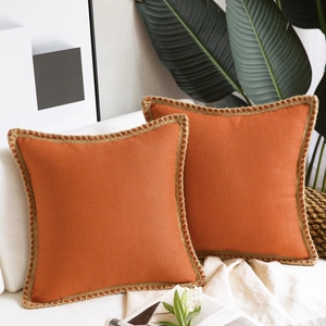 Close-up of orange linen sofa pillow cases with woven jute trim on a cozy couch