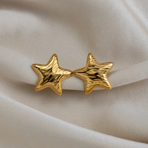 Macro detail of textured 18K gold-plated star studs on a beige fabric background