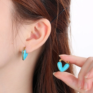 Detailed view of turquoise heart earring with gold plating shown worn on an ear