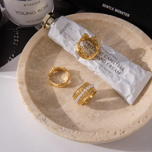Three gold stainless steel rings with crown, pearls, and beaded textures on stone tray