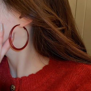 Close-up of a large glossy reddish-brown resin hoop earring worn by a model in style