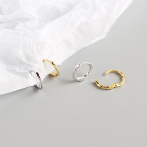 Detailed view of gold and silver twisted hoop earrings on textured white paper