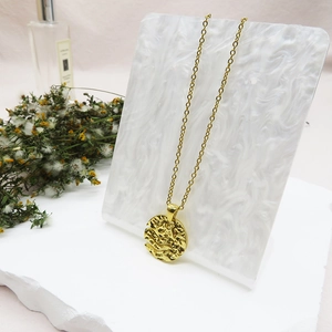 Macro shot of 18K gold-plated necklace with hammered round pendant on marble background