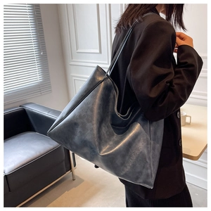 Detail of soft dark gray oil wax leather tote bag with fine shoulder straps on a sofa
