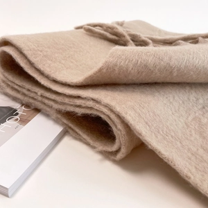 Detail shot of beige mohair scarf with soft plush texture and fringe tassels on a magazine