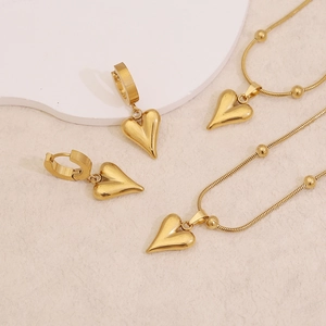 Minimalist gold heart pendant necklace and earring set on white textured background
