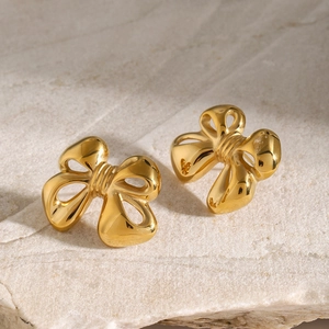 Macro detail of 18k gold-plated stainless steel bow earrings on a natural stone surface