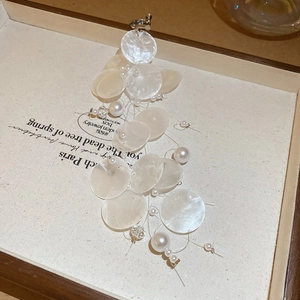 Detailed close-up of shell disc tassel earrings with white pearls on a display tray