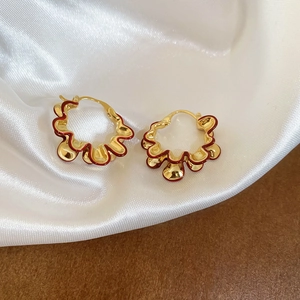 Detail of vintage golden hoop earrings with red wavy enamel on soft silk background
