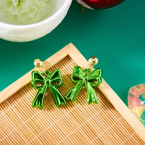 Detailed top view of green metallic bow earrings on a bamboo tray with festive decor