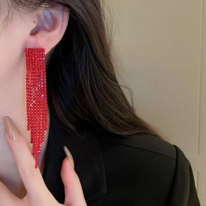 Detailed view of long red rhinestone tassel earrings showing dramatic drape on model