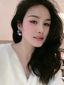 Macro shot of lily flower pearl earring with rhinestones worn by a model in white sweater