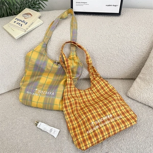 Detail of embroidered plaid canvas tote bags with SOZAKKA logo on a soft grey sofa