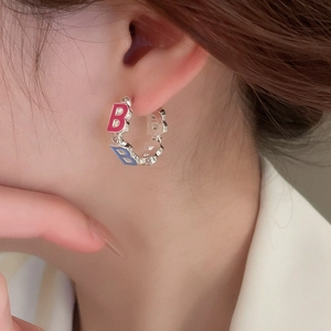Silver letter B hoop earrings with pink and blue enamel inlay worn by a model