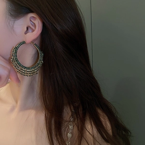 Dettaglio di orecchini a cerchio dorati a strati con strass verde smeraldo su modella