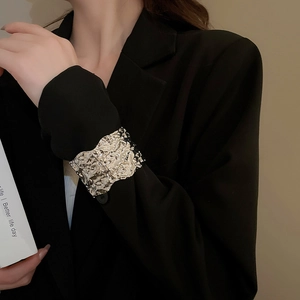 Detailed view of wide irregular wrinkled metal cuff bracelet over a black blazer sleeve