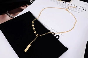 Close-up of 18K gold plated bar pendant on coffee bean link chain over fashion magazines